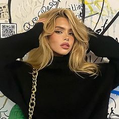 a woman with blonde hair wearing a black turtle neck sweater and gold chain bracelets