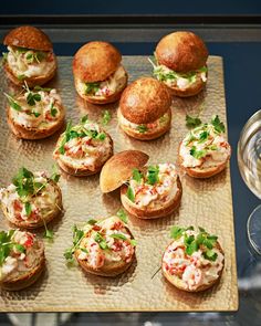 small sandwiches and rolls on a tray next to a glass of wine, with garnishes