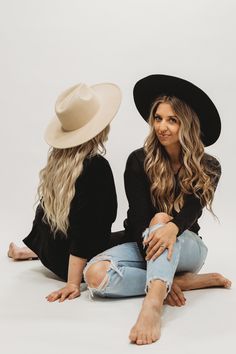 two women sitting on the ground with hats on their heads and one is wearing ripped jeans