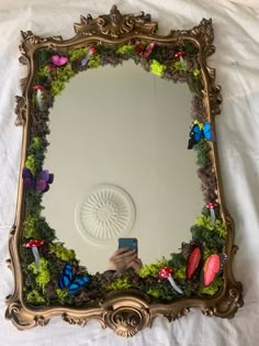 a mirror that is sitting on top of a white sheet with flowers and butterflies around it