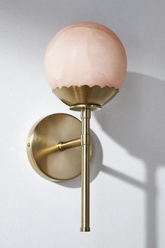 a wall mounted light with a pink glass shade on it's face and arm