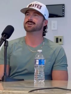 a man in a baseball cap is sitting at a table with a water bottle and microphone