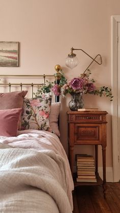 a bed room with a neatly made bed next to a night stand and flowers on the nightstand