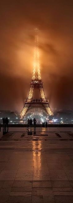 the eiffel tower lit up at night with people standing in front of it