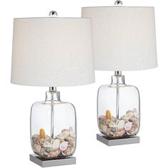 two clear glass lamps with shells in them on a metal base and a white lamp shade