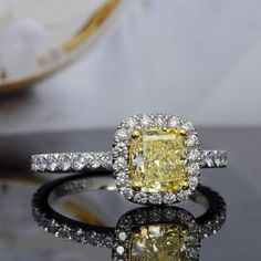 a fancy yellow diamond ring on a black surface with white diamonds around the band and center stone