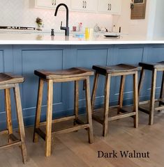 three wooden stools sitting in front of a kitchen island with white cabinets and blue walls