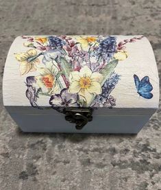 a white box with flowers and butterflies painted on the lid sitting on a stone surface