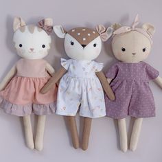 three little stuffed animals are lined up on a white surface, one is wearing a dress and the other has a pink polka dot headband