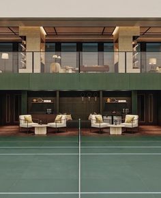 a tennis court with couches and tables in front of a large glass windowed building