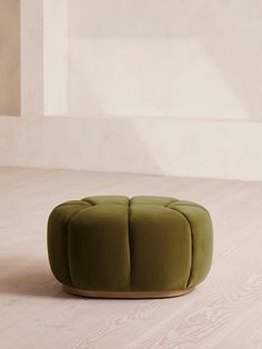 a green ottoman sitting on top of a hard wood floor next to a white wall