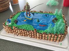 there is a cake that looks like a fishing scene on the lake and man in boat