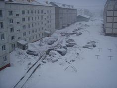 cars are parked on the snow covered street in front of buildings and apartment buildings, as seen from above