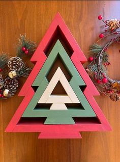 a christmas tree made out of wooden blocks on a table next to wreaths and pine cones