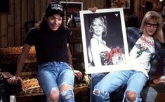 two people sitting on a couch, one holding a framed photo and the other wearing ripped jeans