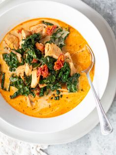 a bowl of soup with spinach, chicken and tomatoes in it on a white plate