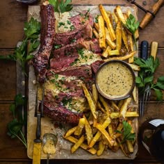 steak, french fries and sauce on a cutting board with utensils next to it