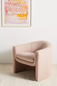 a beige chair sitting in front of a painting on the wall next to a white rug