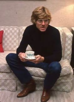 a man sitting on a couch holding a cup and saucer