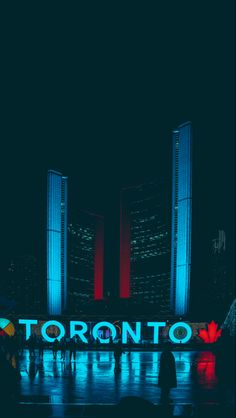 people standing in front of the toronto sign lit up with red and blue lights at night