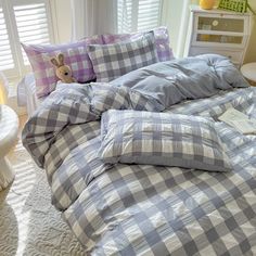 an unmade bed with blue and white checkered comforter, pillows and stuffed animal