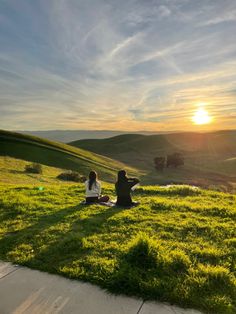 two people are sitting in the grass on a hill at sunset with their backs to each other