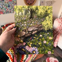 a person holding up a card with flowers and trees in the background on a table