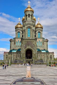 an ornate building with gold domes on it's sides and people walking around in front