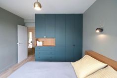 a bedroom with blue walls and white bedding, wooden headboard, and built in cupboards