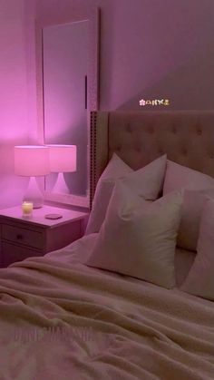 a bed with white sheets and pillows in a pink lit up room, next to a night stand