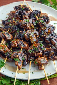 several skewers of meat and vegetables are on a white plate with green garnishes