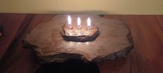 a small birthday cake with lit candles in it on a wooden table next to a wall