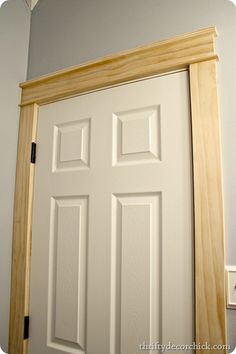 a white door with wooden frame in front of a gray wall and light fixture on the ceiling