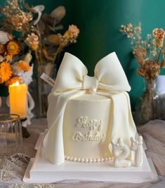 a white cake with a bow on top sitting on a table next to flowers and candles