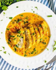 a white plate topped with chicken and yellow curry next to a fork on a blue and white striped table cloth