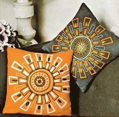 two decorative pillows sitting on top of a couch next to a vase with flowers in it