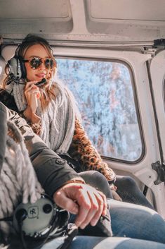 two people sitting in the back of an airplane with headphones on and one person holding a cell phone to her ear