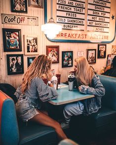 two young women sitting at a table in a diner eating and drinking sodas together