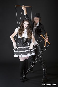 two people dressed up in costumes with sticks and poles attached to their backs, standing against a black background