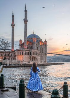 a woman is standing on the dock in front of a large building with two towers