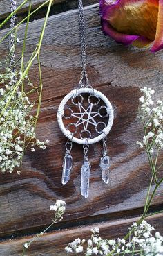 a small white dream catcher with crystals hanging from it's chain next to flowers