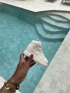 a hand holding up a pair of white sneakers next to a swimming pool