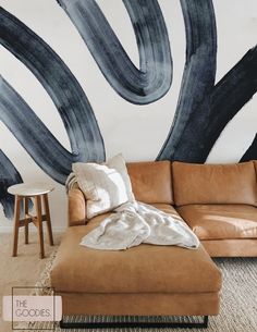 a couch and ottoman in front of a wall with an artistic painting on it's side