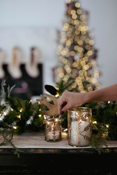 two candles on a table with christmas lights in the background and a person decorating them