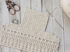 a crocheted piece of cloth next to a pair of scissors on a wooden table