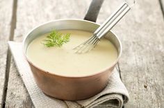 a pot filled with soup sitting on top of a wooden table next to a whisk