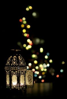 a lit lantern sitting on top of a table in front of a tree filled with lights