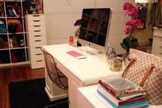 a white desk topped with a computer monitor next to a book shelf filled with books