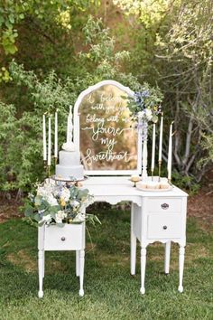 a wedding cake sitting on top of a white table next to a mirror and candles