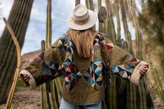 a woman standing in front of a cactus with her arms spread out and wearing a hat